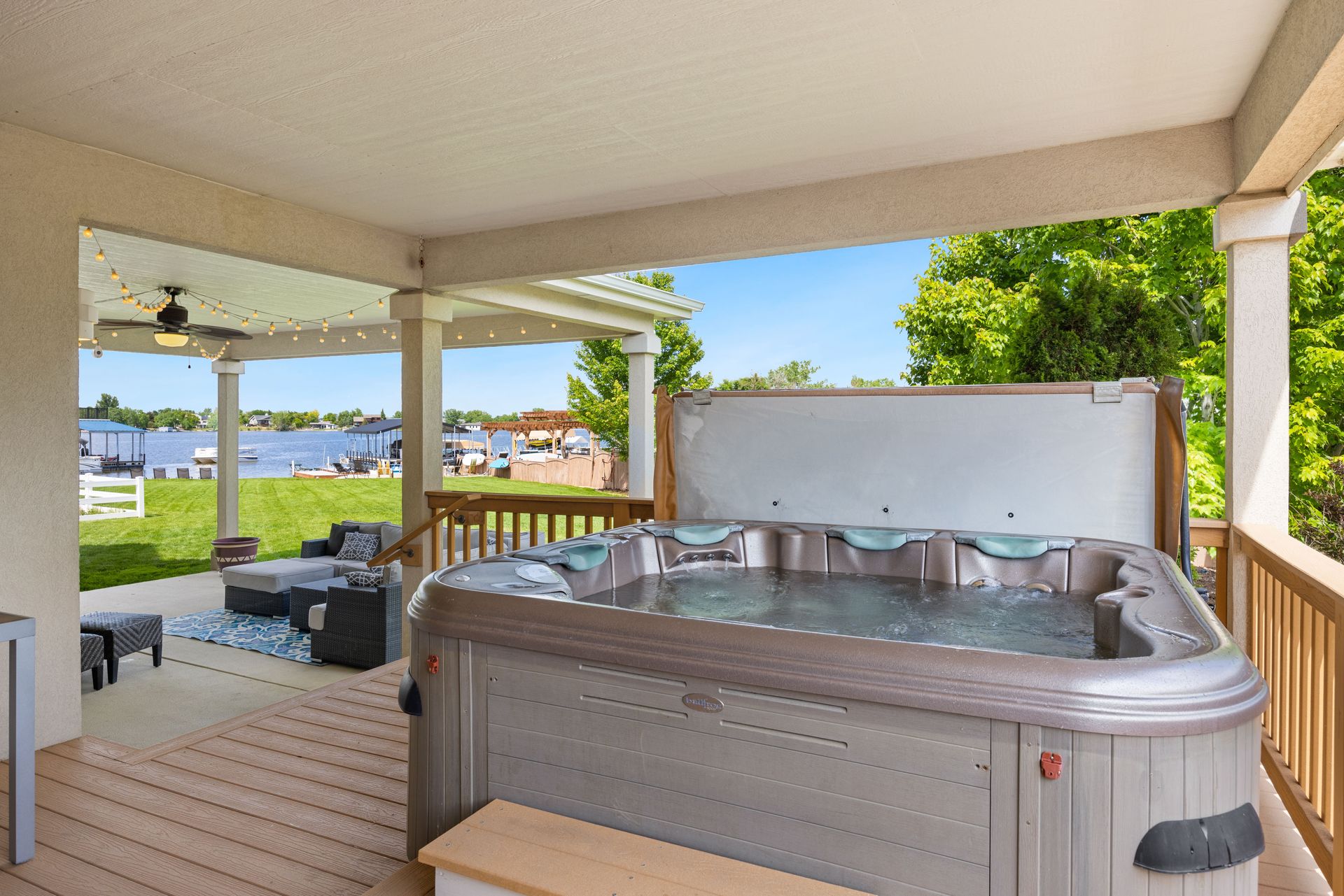 Explore a serene outdoor patio featuring a luxurious hot tub overlooking a tranquil lake.